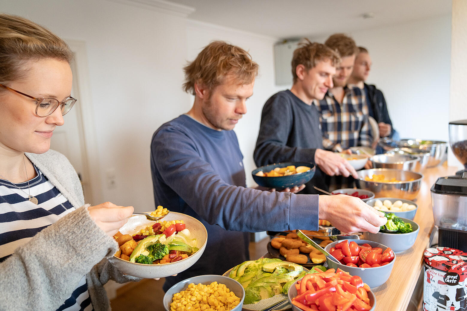 Mitarbeitende von visuellverstehen an der Salatbar in der Küche füllen sich verschiedene bunte Salatzutaten auf ihre Teller.