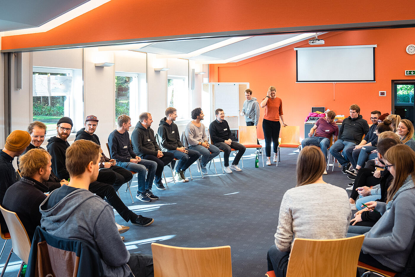 Das Team von visuellverstehen bei der Klausurtagung 2021 in einem großen, orange tapezierten Raum im Stuhlkreis.