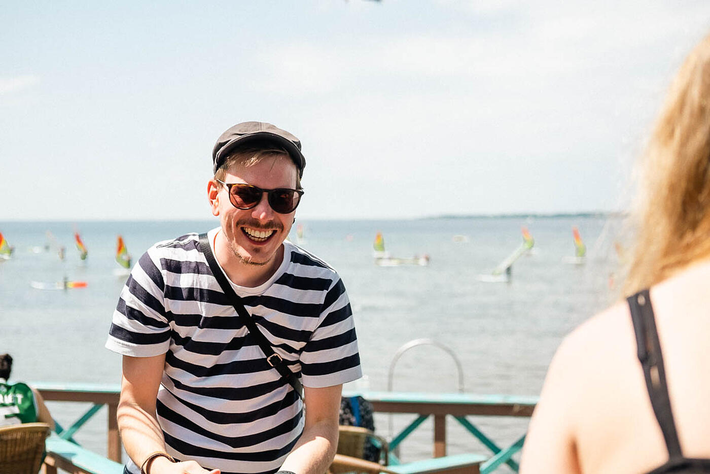 Ein Mitarbeiter von visuellverstehen lachend in der Sonne, er trägt ein gestreiftes Shirt.