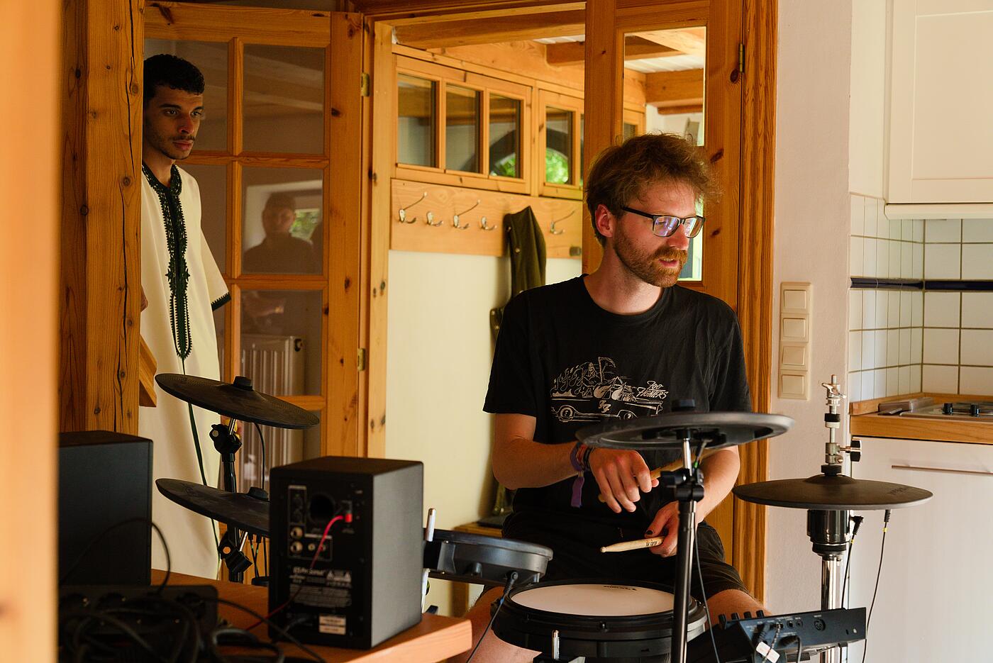 Ein Mitarbeiter spielt in einem warm erleuchteten Innenraum Schlagzeug an einem E-Drum-Set.