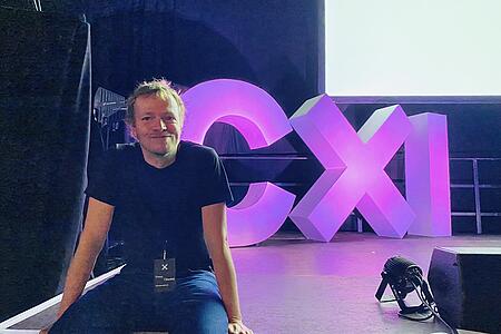 Ein Mitarbeiter von visuellverstehen sitzt auf einem Bühnenrand, im Hintergrund die großen CXI-Lettern.