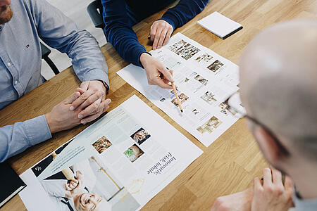 Mitarbeitende von visuellverstehen sitzen an einem Tisch, auf dem Werbematerialien für eine Kochschule ausgebreitet sind.