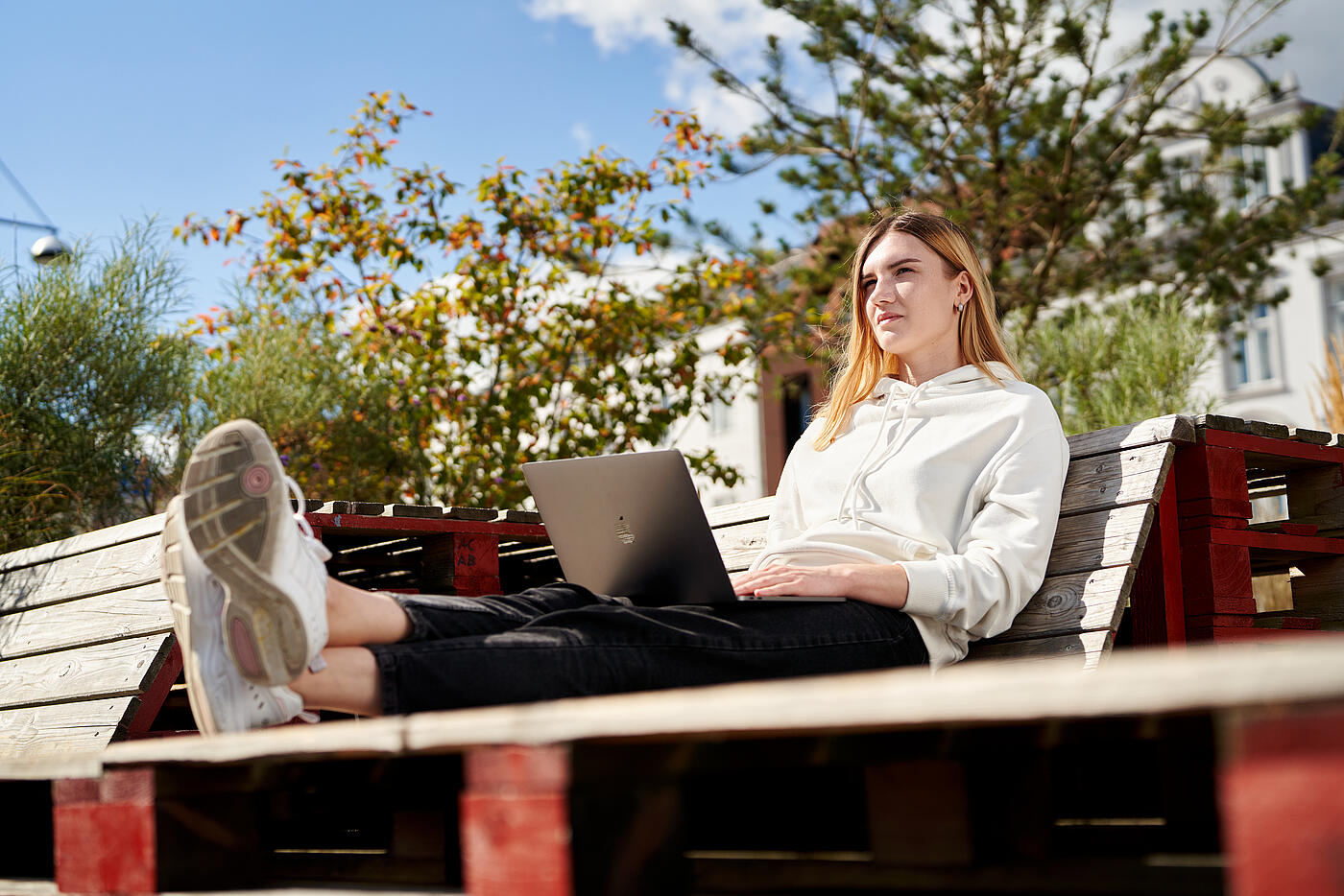Eine Mitarbeiterin von visuellverstehen sitzt am Flensburger Hafen in der Sonne und arbeitet am Macbook.