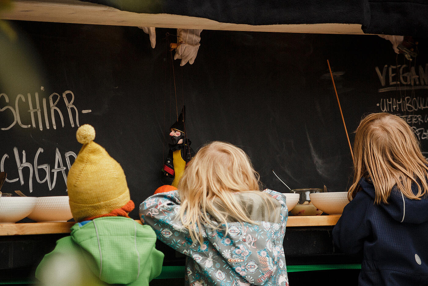 Drei Kinder beobachten ein Puppentheater.
