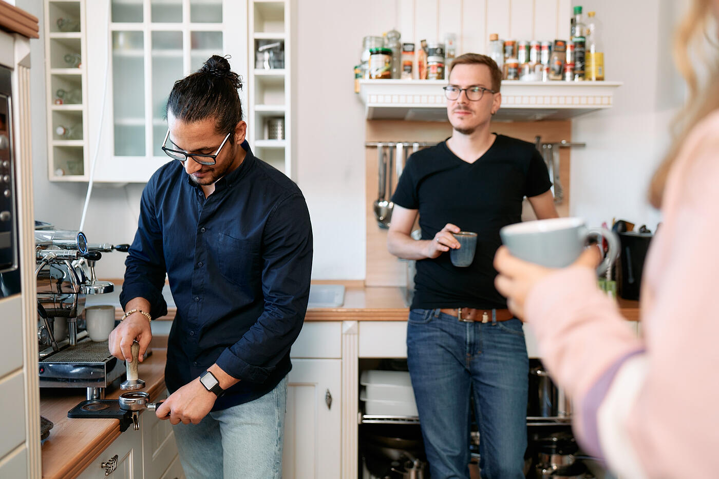 Drei Mitarbeitende von visuellverstehen, die sich an der Kaffeemaschine in der modernen, hellen Küche treffen.