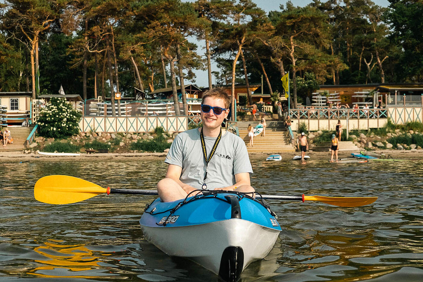 Ein Mitarbeiter von visuellverstehen im Kajak auf dem Wasser, hinter ihm der Strand und Nadelbäume.