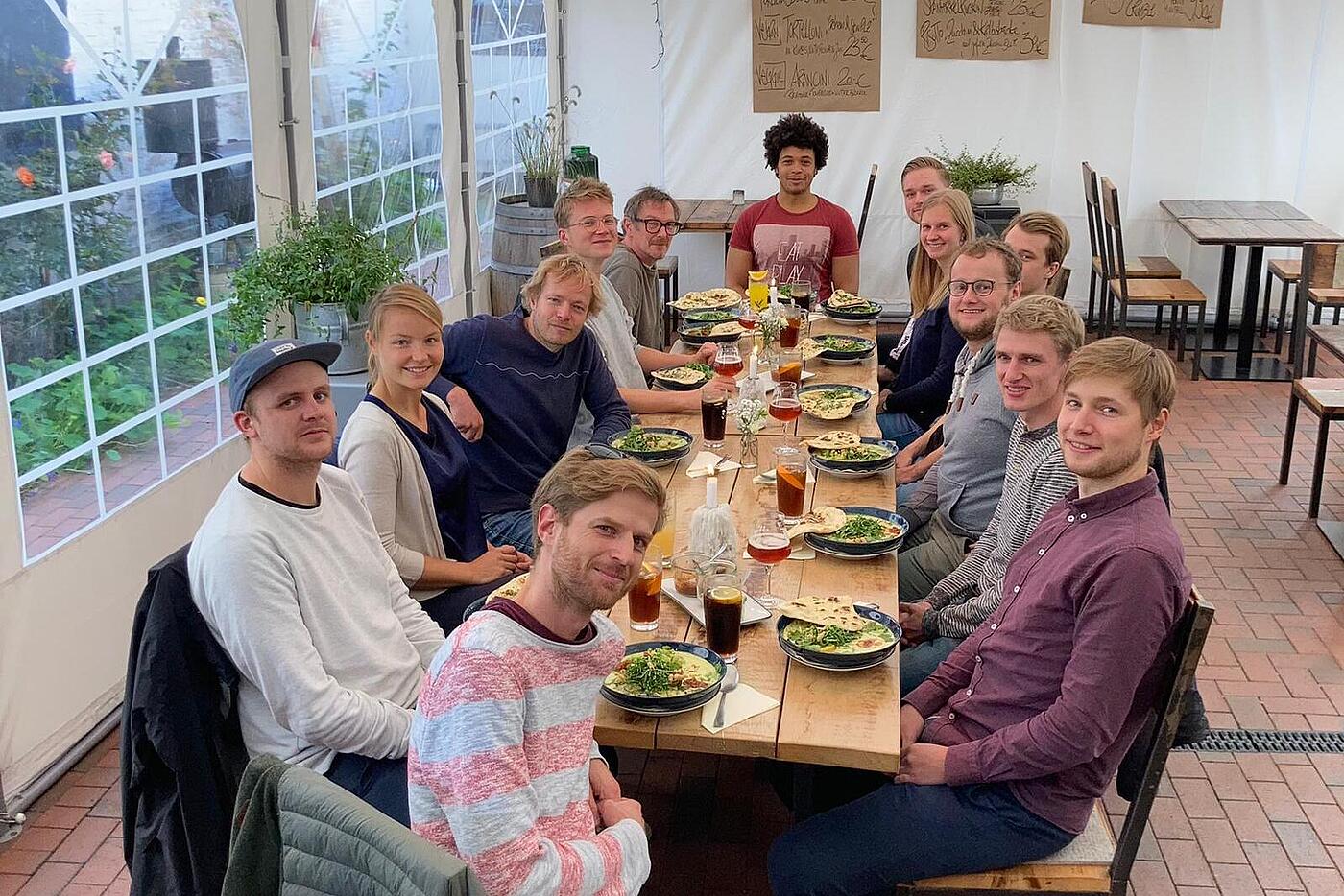 Das visuellverstehen-Team sitzt auf der Terrasse eines feinen Restaurants in einem Veranstaltungszelt, gefüllte Teller vor sich.