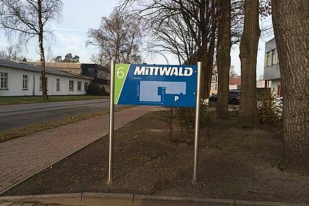 Am Wegesrand steht ein blaugrünes Schild mit der Aufschrift Mittwald.