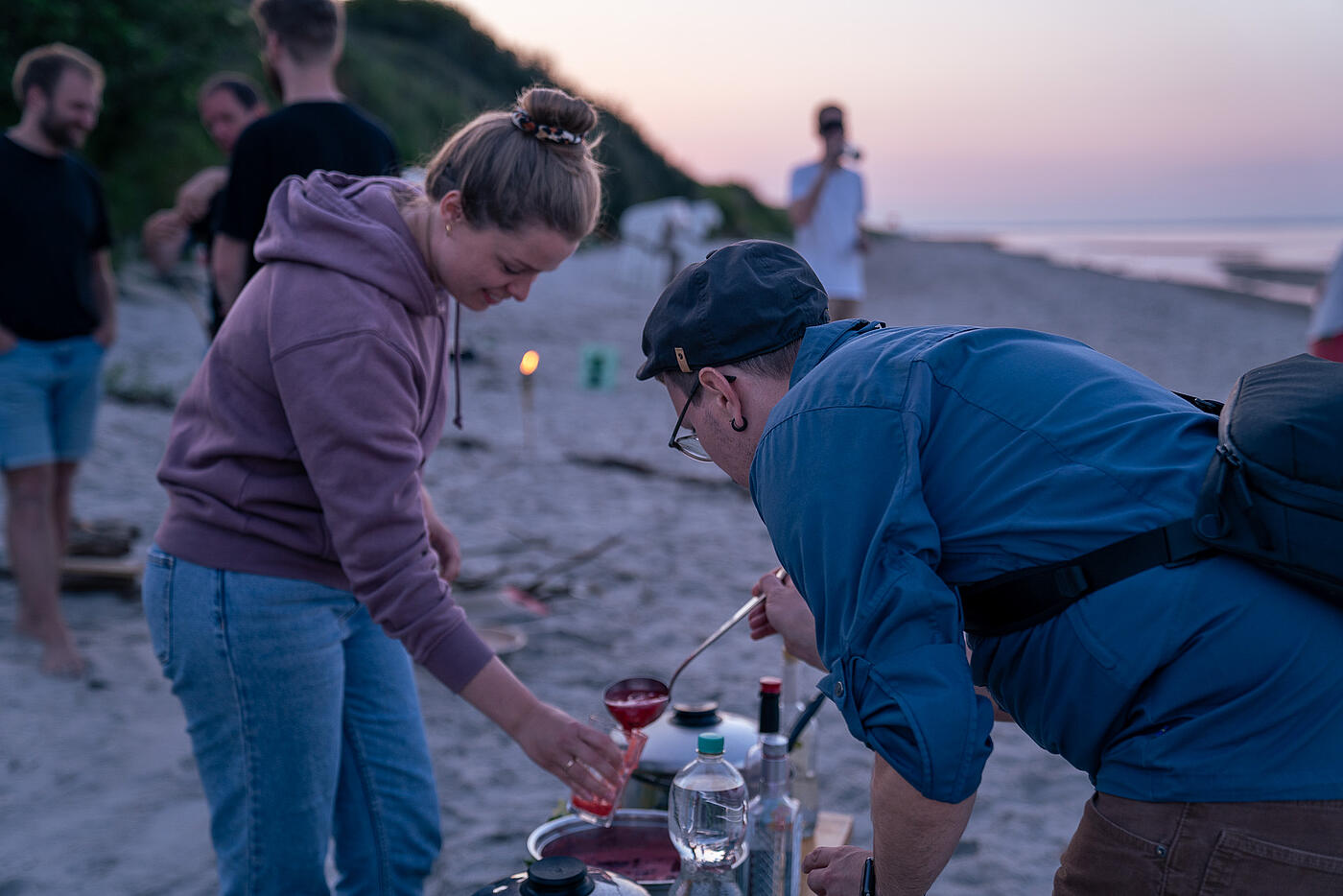 Mitarbeitende von visuellverstehen füllen sich am Strand ein rotes Getränk in ihre Gläser und lachen.