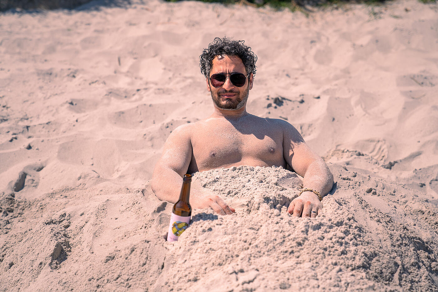 Ein Mitarbeiter von visuellverstehen hat sich im Sand eingebuddelt und schaut in die Sonne.