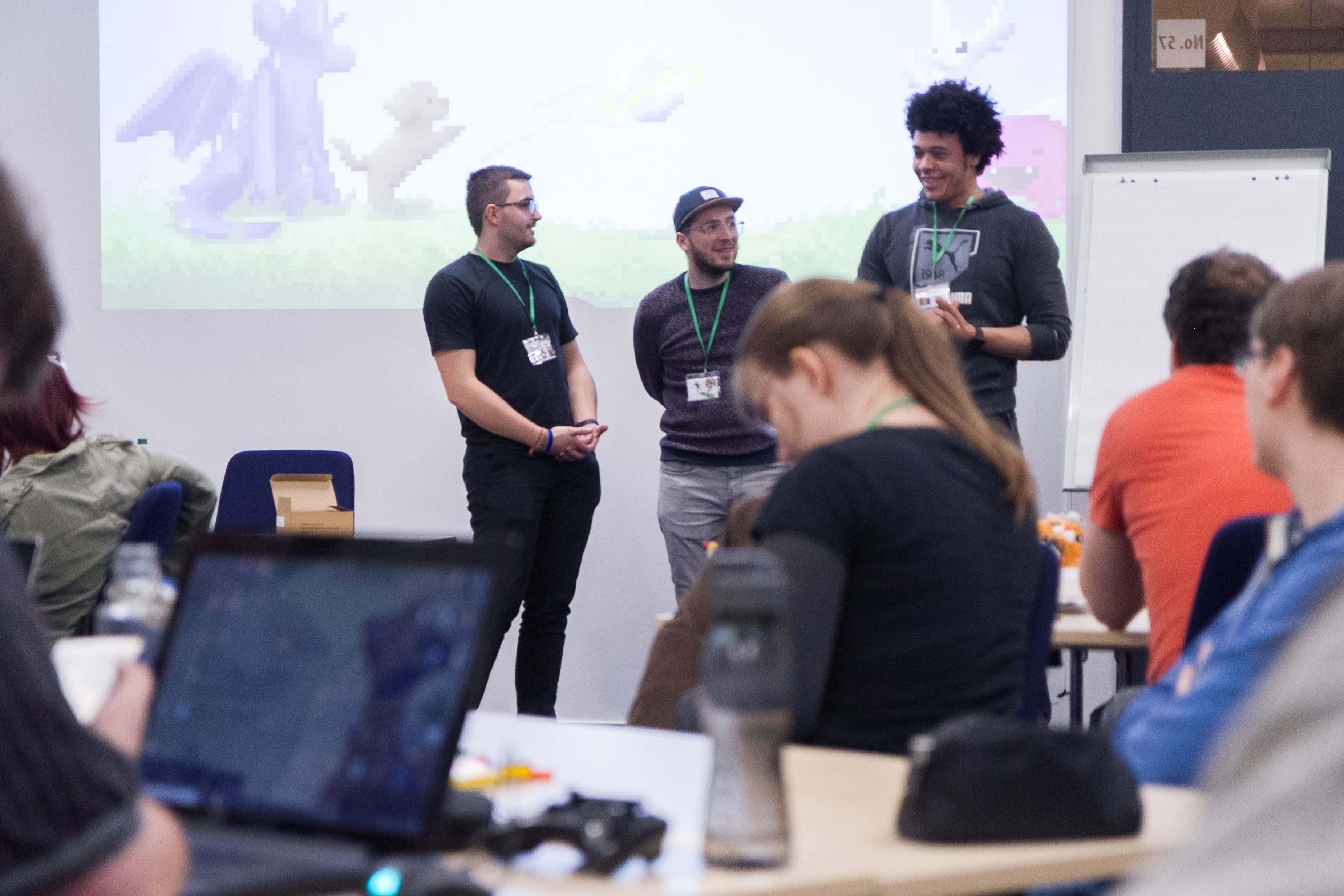 Mehrere Personen halten sich in den Räumen beim Global Game Jam auf, unterhalten sich oder arbeiten am Laptop.