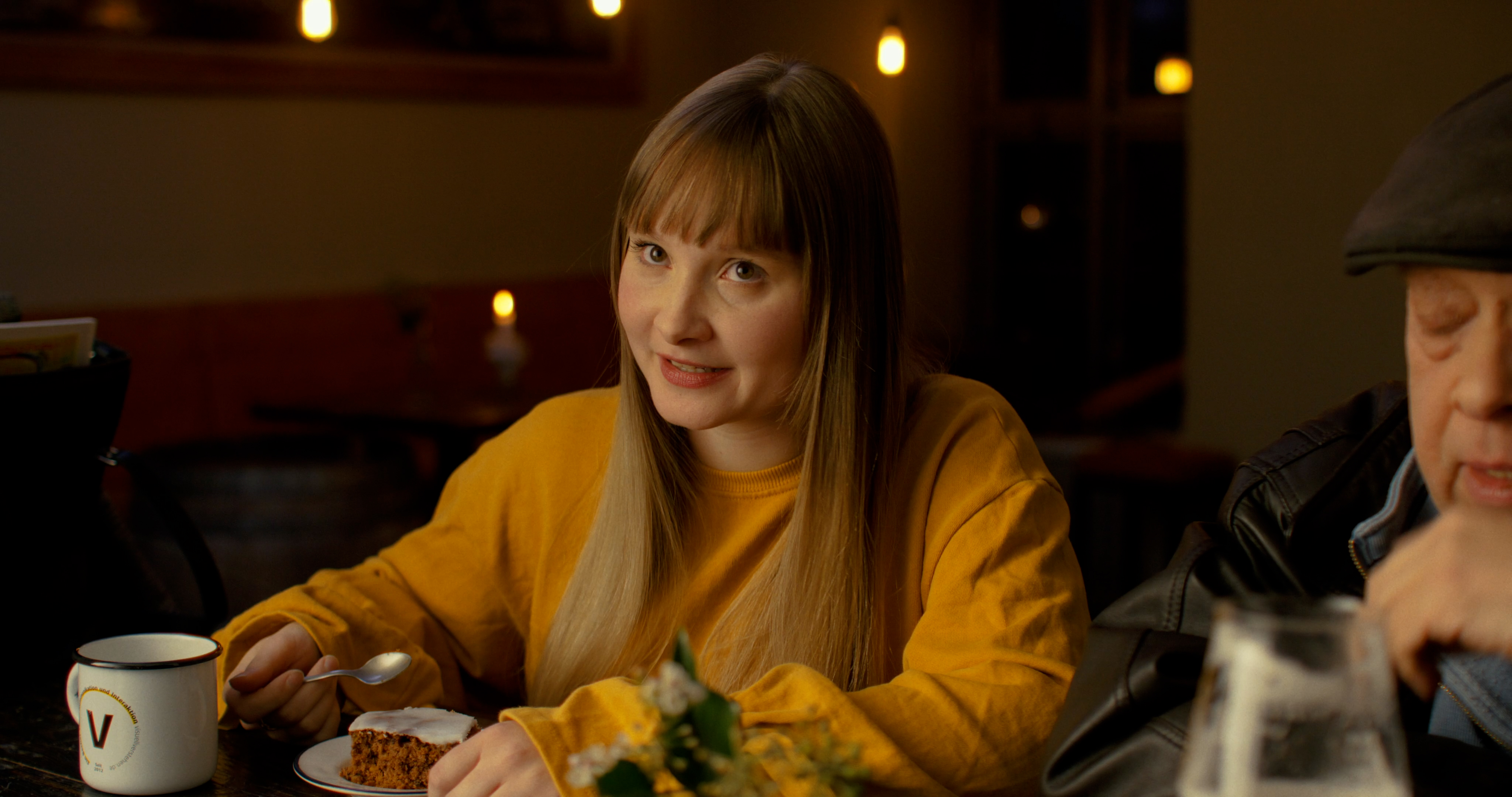 Schauspielerin aus dem visuellverstehen-Jahresrückblick-Video von 2021, die im gelben Pullover an einer Bar sitzt..