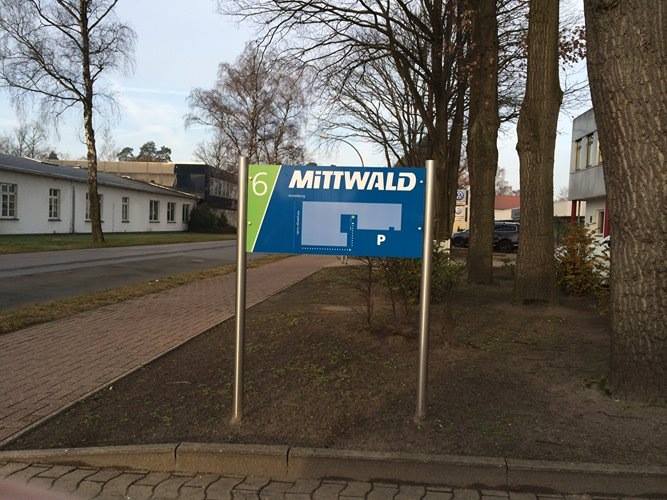 Am Wegesrand steht ein blaugrünes Schild mit der Aufschrift Mittwald.