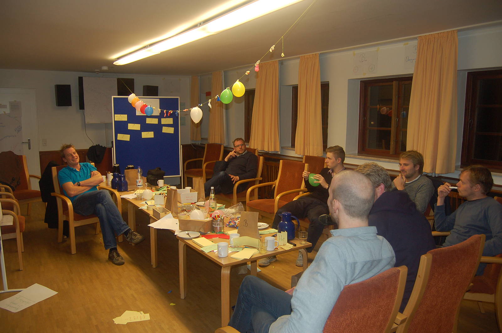 Mitarbeitende von visuellverstehen sitzen abends in einem Besprechungsraum. Es hängen Luftballons von der Decke.