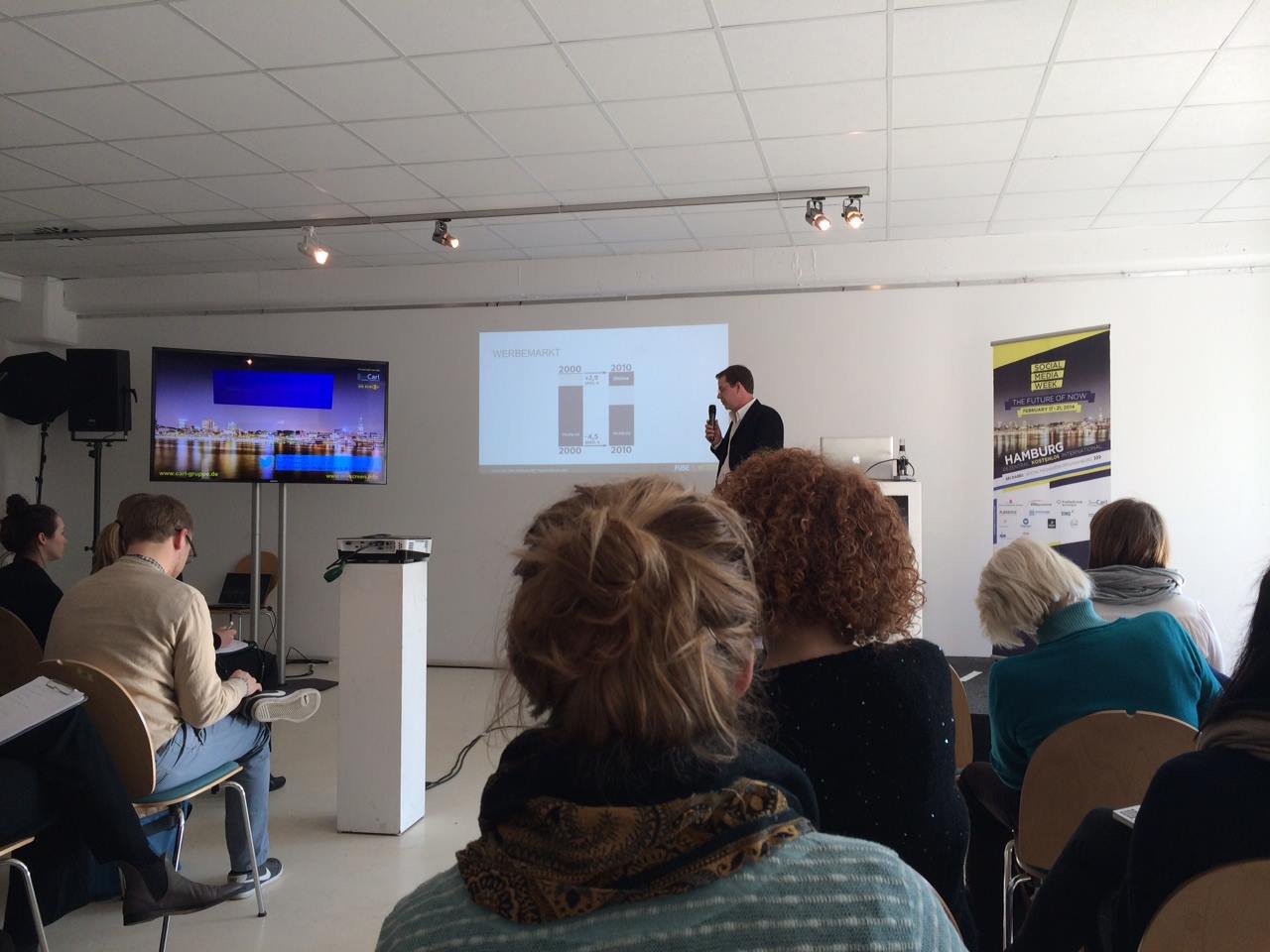 Viele Personen verfolgen bei der Social-Media-Week in Hamburg den Vortrag eines Dozenten in einem hellen Raum.