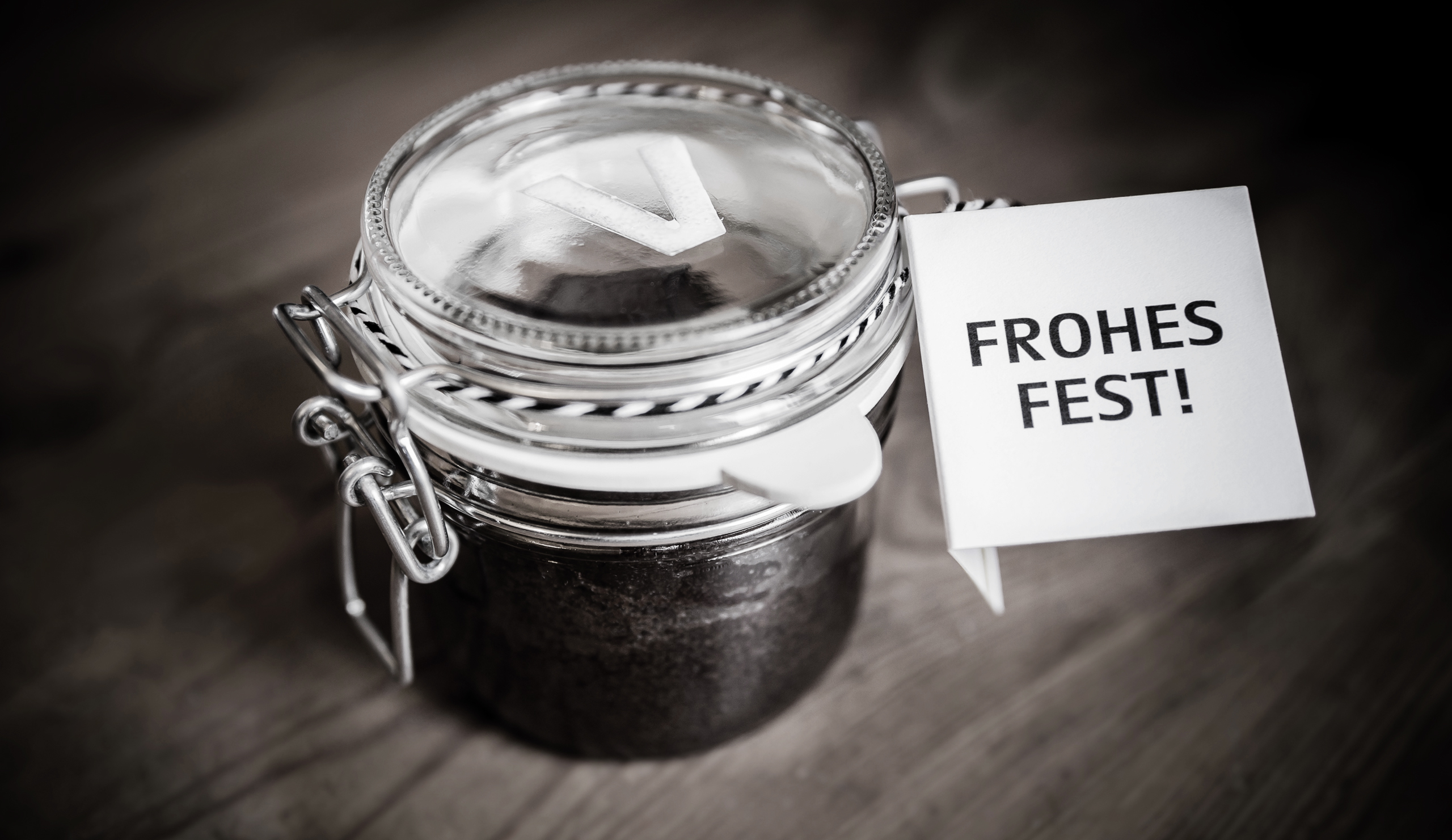 Auf einem Holztisch steht ein Einmachglas mit einer "Frohes Fest"-Karte daneben.